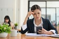 Serious young Asian businesswoman at her office desk dealing with a smartphone problem Royalty Free Stock Photo