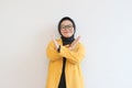 serious young Asian Muslim woman wearing glasses and yellow blazer crossing hands makes stop gesture and demonstrates rejection Royalty Free Stock Photo