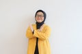 serious young Asian Muslim woman wearing glasses and yellow blazer crossing hands makes stop gesture and demonstrates rejection Royalty Free Stock Photo