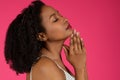 Serious young black curly lady enjoy beauty care at empty space isolated on pink background, studio