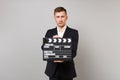 Serious young business man in classic black suit, shirt holding classic black film making clapperboard isolated on grey Royalty Free Stock Photo