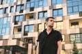 Serious young business man standing on urban background. Guy model in black shirt stands against the background of a modern Royalty Free Stock Photo