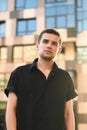 Serious young business man standing on urban background and looking into camera. Guy model in a black shirt stands against the Royalty Free Stock Photo