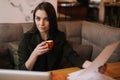 Serious young business woman studying paper documents in cafe sitting at table with laptop. Royalty Free Stock Photo