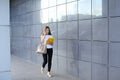 Serious young business woman walks and talks on phone, holds and looks at documents and smiling on background of wall of Royalty Free Stock Photo