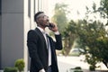 Serious young businessman in black suit standing and talking on cell phone near business center Royalty Free Stock Photo