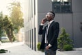 Serious young businessman in black suit standing and talking on cell phone near business center Royalty Free Stock Photo