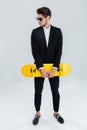 Serious young businessman holding yellow skateboard