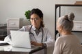 Serious young female doctor meeting with elderly patient in office