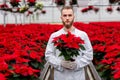 Serious young gardener in a greenhouse. A man in uniform holds a pot of red poinsettia. Gardening concept