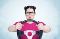 Serious young girl in glasses and t-shirt with steering wheel on light blue smoke background, car driver concept Royalty Free Stock Photo