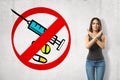 Serious young girl with hands crossed, standing against wall with picture of syringe and some meds enclosed in red