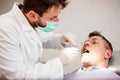 Serious young male dentist examining mature male patient