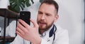 Serious young male doctor consults remote patient on coronavirus quarantine using smart phone video call app at office. Royalty Free Stock Photo