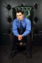 Serious young man in blue sits in leather armchair