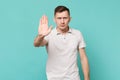 Serious young man in casual clothes standing and showing stop gesture with palm isolated on blue turquoise wall Royalty Free Stock Photo