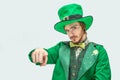 Serious young man in green suit point straight on camera. He wear St. Patrick`s costume. on grey background.