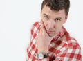 Serious young man in hipster shirt holding hand on chin and standing against white background Royalty Free Stock Photo