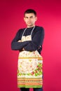 Serious young man in a kitchen apron on a pink background. The concept of gender stereotypes