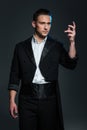Serious young man magician in black tail coat showing tricks