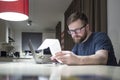 Young man managing finances sitting at home in the kitchen near the laptop and looking at the receipt Royalty Free Stock Photo