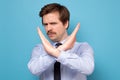 Serious young man in shirt showing stop sign crossing hands and looking at camera Royalty Free Stock Photo