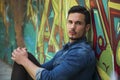 Serious young man sitting against colorful graffiti wall Royalty Free Stock Photo