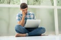 Serious young man sitting on floor working with laptop computer on window at home . Bored worker tired from work at home office di Royalty Free Stock Photo