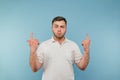 Serious young man in a white T-shirt stands on a blue background with a serious face and points his fingers up on an empty seat Royalty Free Stock Photo