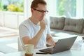 Serious young man working online with laptop at home, holding paper sitting at office desk Royalty Free Stock Photo