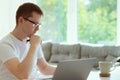 Serious young man working online with laptop at home, holding paper sitting at office desk Royalty Free Stock Photo