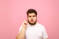 Serious young overweight man in white t-shirt, isolated on a pink background, looks into the camera with a surprised face and Royalty Free Stock Photo
