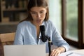 Serious young 20s millennial girl speaking at microphone at laptop