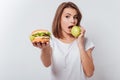 Serious young woman holding fastfood and eating apple