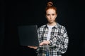 Serious young woman holding laptop computer and looking at camera on isolated black background. Royalty Free Stock Photo