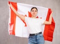 Serious young woman holding state flag of Canada against gray wall background indoors