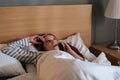 Serious young woman lying on cosy bed at home and talking mobile phone before bedtime in evening at home. Royalty Free Stock Photo