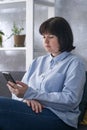 Serious young woman is sitting on the couch with a phone in her hands. Business Woman solves work issues. Smm manager