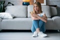 Serious young woman using her mobile phone while sitting on the floor in the living room at home Royalty Free Stock Photo