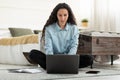 Serious young woman using laptop, having remote job, sitting on floor in bedroom, full length Royalty Free Stock Photo