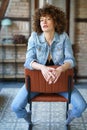 Serious young woman wearing denim jacket sitting on leather chair Royalty Free Stock Photo