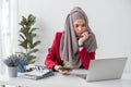 Serious young woman wearing hijab sitting at desk working on new business project alone in modern office Royalty Free Stock Photo