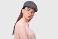 Serious young woman wears transparent spectacles, casual pink shirt and gray cap, looks seriously directly into the camera, poses Royalty Free Stock Photo