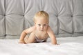 Seriuos baby boy crawling on the bed. Concentrated toddler on the white blanket