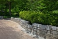 Serpentine rustic granite stone retaining wall in a public park, green trees and bushes, hexagonal paver blocks Royalty Free Stock Photo
