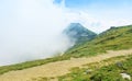 A serpentine track road narrow path at mountainside going up around a top of a hill and a big fog cloud moving at the background Royalty Free Stock Photo