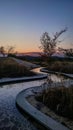 Serpentine walkway at dusk with reflective water and tree silhouette