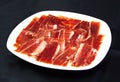 Serrano ham slices on a white dish over black