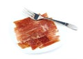 Serrano ham on a white dish with a metal fork. Jabugo. Spanish tapa.