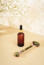 Serum bottle and jade facial roller on neutral beige background with gypsophila flowers, close up Royalty Free Stock Photo